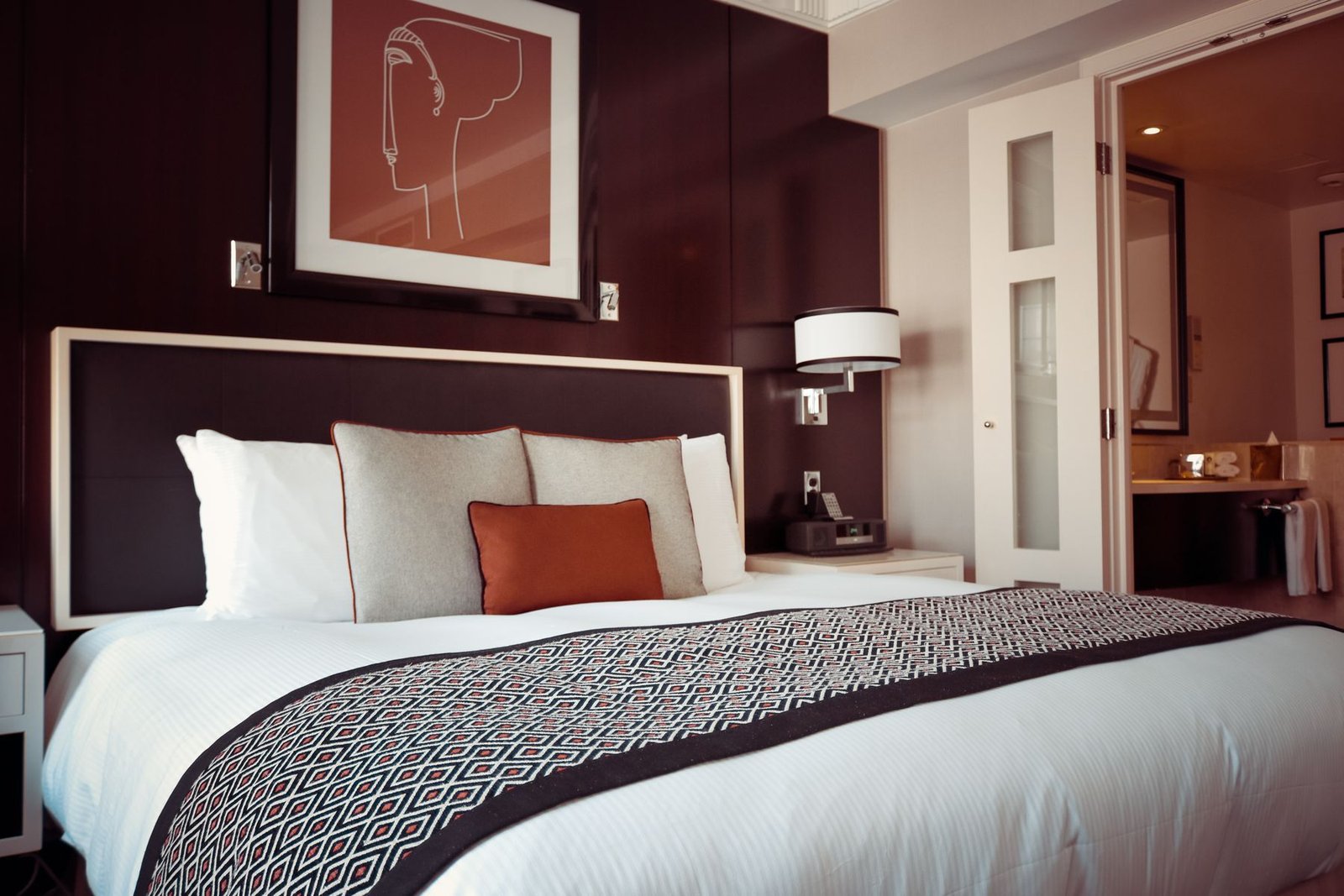 A welcoming hotel room with a neatly made bed, warm wood panelling and a bedside lamp